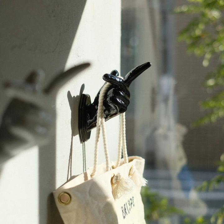 フレミングの手の形をした黒い陶器のオブジェ。白い壁にとり付けられており、白い布性のトートバッグが掛けられている。