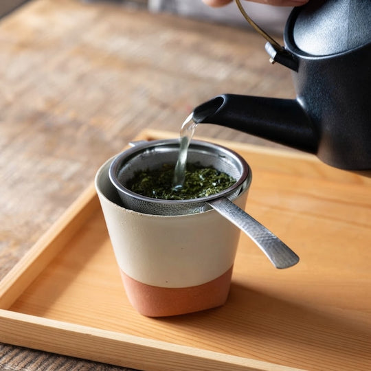 燕三条 ハンドル付き茶こし なごみ槌目 抹茶対応 日本製 日本 現行品 陶器のカップに茶こしをのせて鉄瓶から緑茶を注ぎ茶葉を漉している様子